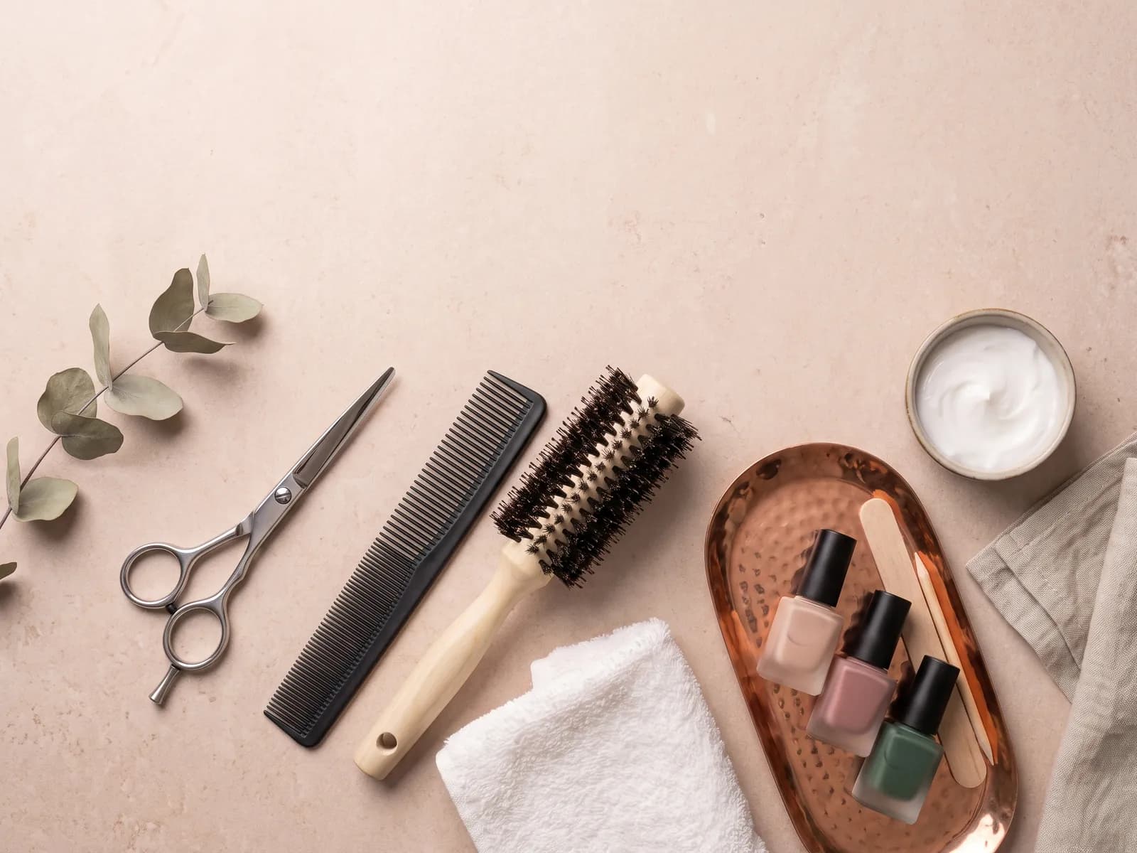 Symbolbild: Friseur- und Kosmetikwerkzeuge auf hellem Stein — Schere, Kamm, Rundbürste, Handtuch und Nagellackfläschchen.